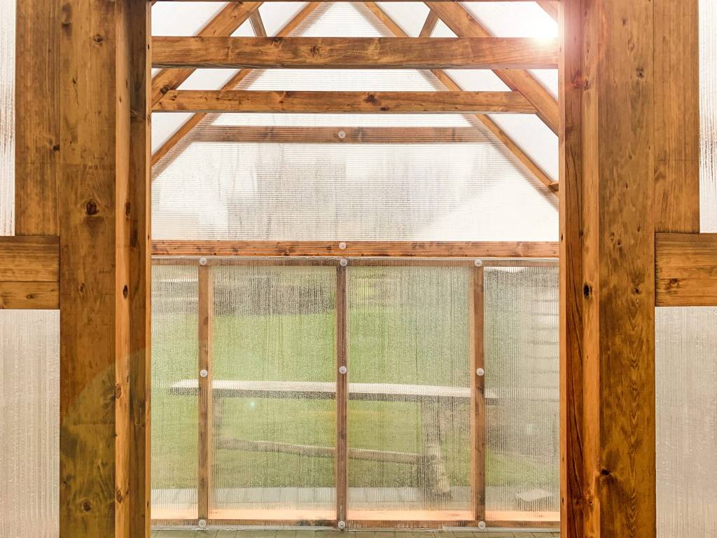 Innenansicht eines gemütlichen Holzgewächshauses mit Holzrahmen und klaren Polycarbonatplatten.